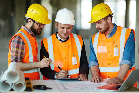 Three contractors in hard hats and hi-vis reviewing plans on site